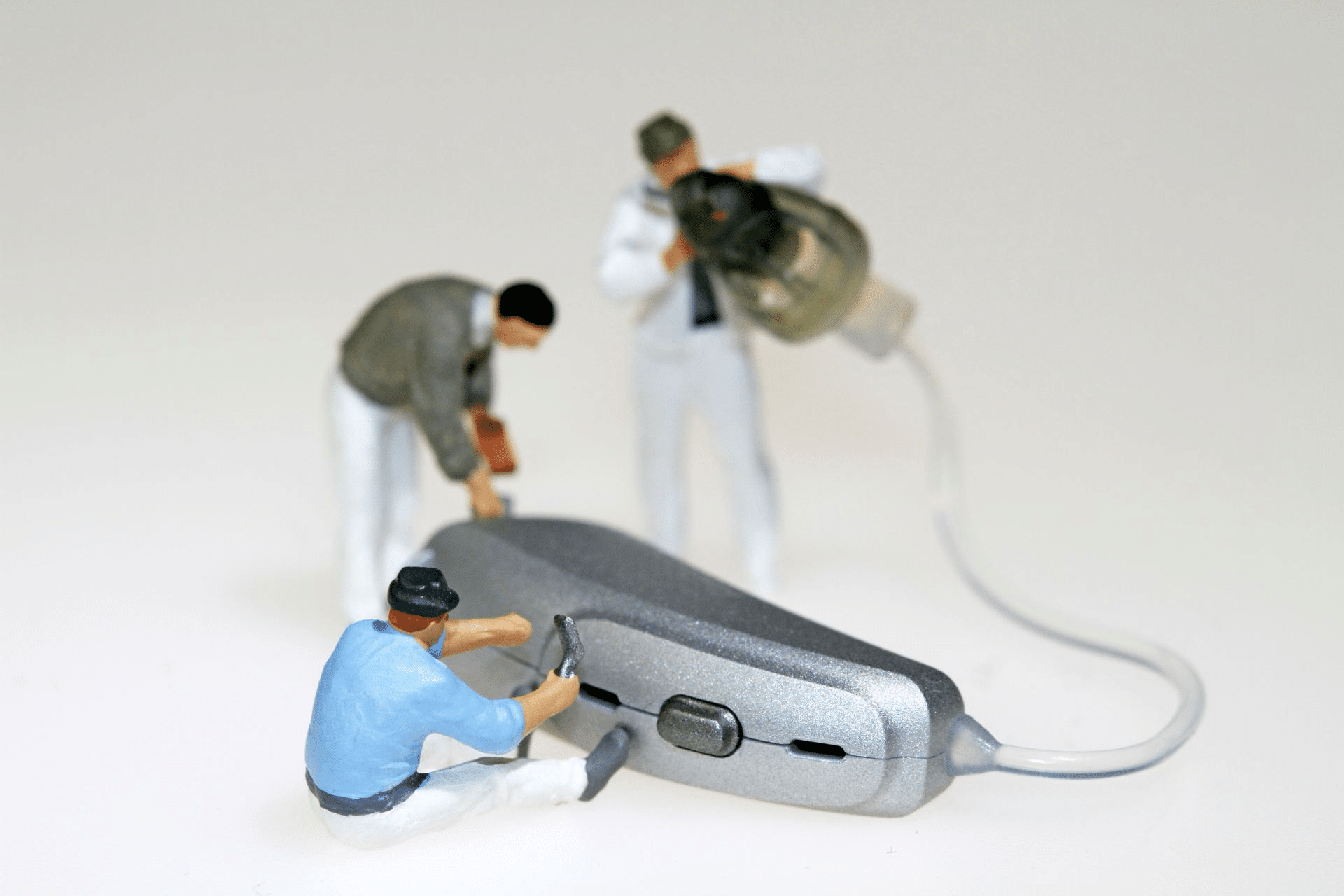 Three miniature figurines doing maintenance work on a hearing aid.
