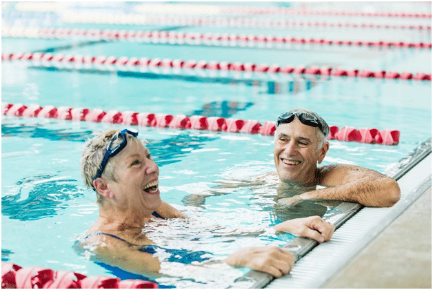 An older couple protect their ears while swimming to avoid swimmers ear infections.